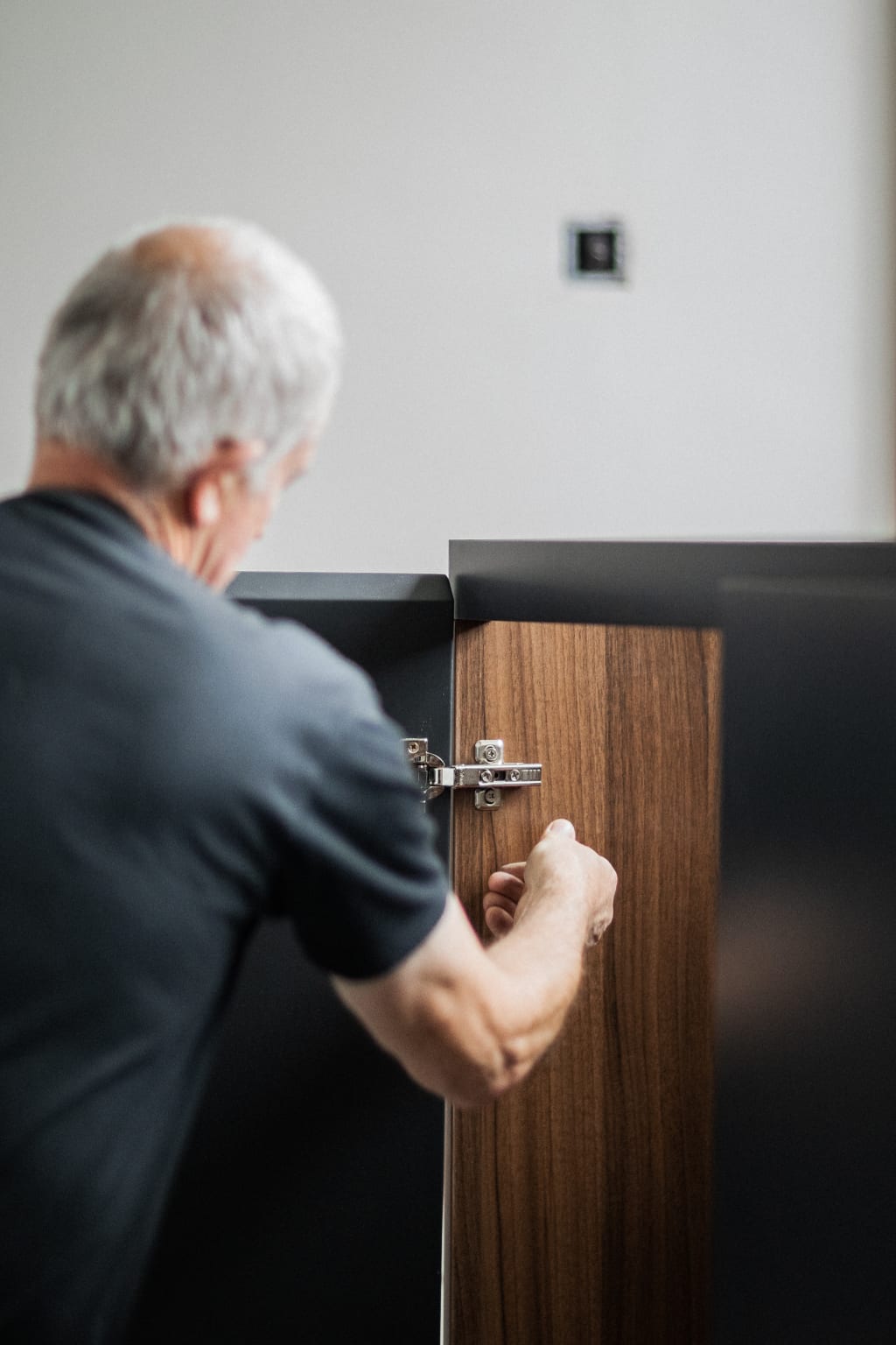 A senior Cymru craftsman fitting a hinge on a walnut cabinet door at the Newport bench
