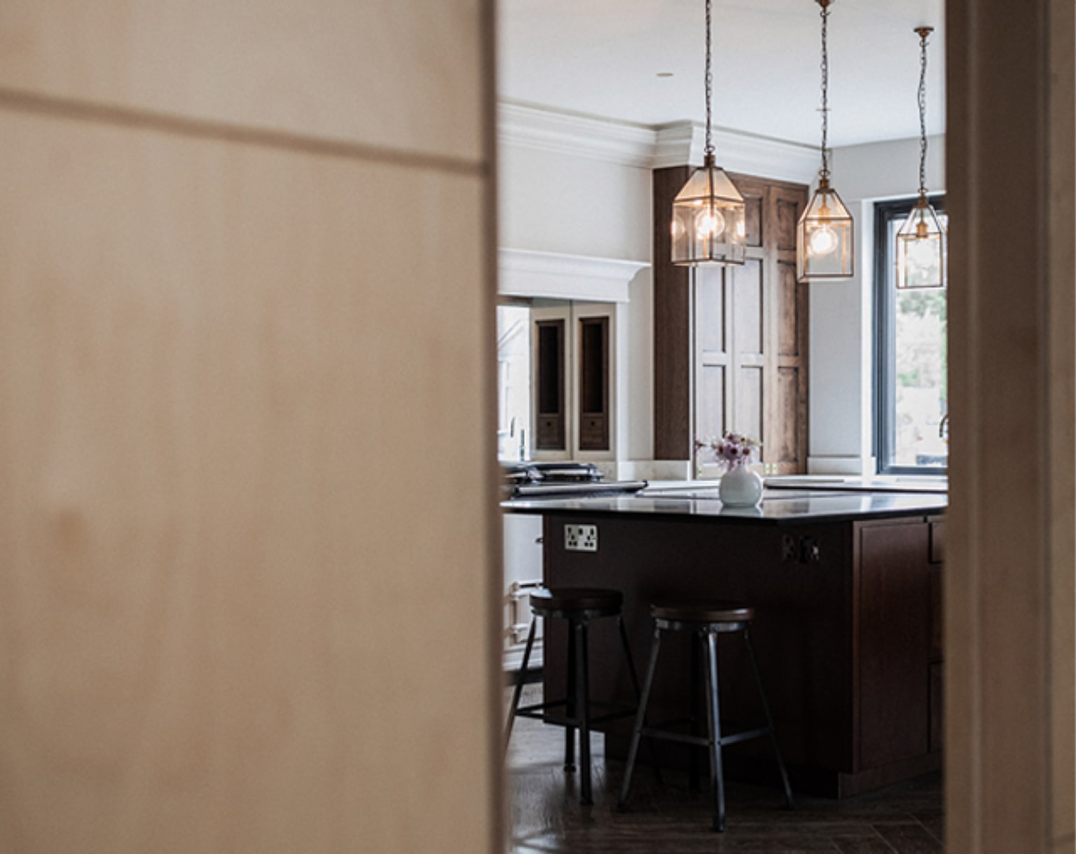 Walnut kitchen with antique lantern pendants, viewed through a partly open door in a Cymru installation